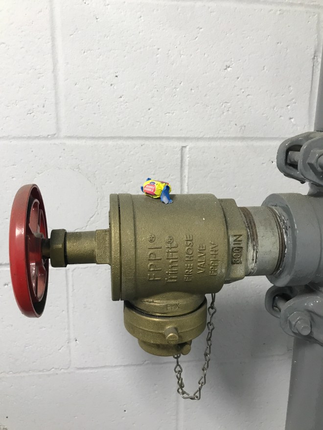 Water access pipe in a stairwell. There's a wrapped piece of candy on top of the shut off valve.