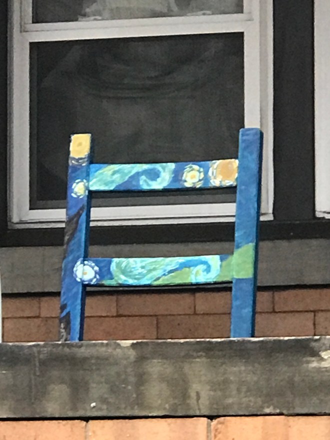 Wooden chair on a porch. Chair is painted in the blue, yellow, and orange colors and patterns of Van Gogh's Starry Night.
